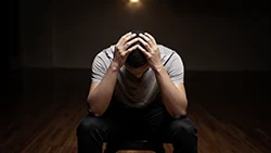 Мужчина сидит на стуле посередине комнаты опустив голову